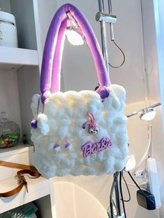 a white purse with purple handles hanging from it's side on a hook in a bathroom