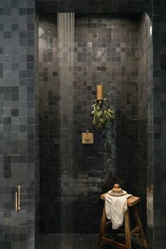 a black tiled shower with a wooden stool and potted plant on the wall next to it