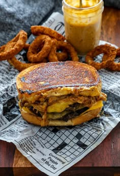 a grilled cheeseburger with onion rings on the side and a cup of mustard