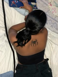 a woman laying in bed with her laptop on her back and spider tattoo on her upper arm