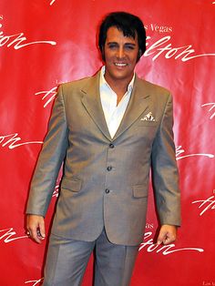 a man standing in front of a red backdrop wearing a gray suit and white shirt