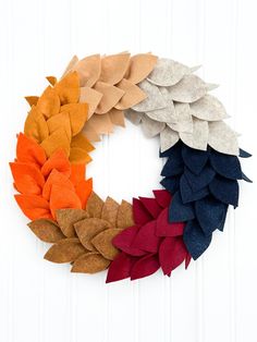 a wreath made out of felt leaves on a white door with the colors of autumn