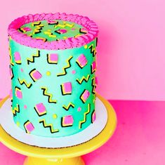 a brightly colored birthday cake on a yellow plate with pink and blue icing, against a pink background