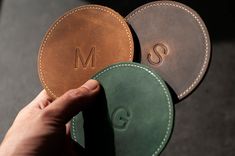 two personalized leather coasters being held by a person's hand with the initials on them