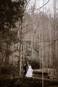 a bride and groom standing on a bridge in the woods