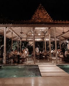 people are sitting at tables under a gazebo by the pool in front of them