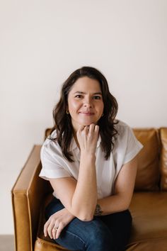 a woman sitting on top of a brown couch next to a white wall and smiling at the camera