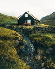 a small black house sitting on top of a lush green hillside next to a stream