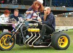 a woman sitting on the back of a motorcycle with two men around her looking at it