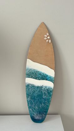 a wooden surfboard sitting on top of a white table next to a wall mounted painting