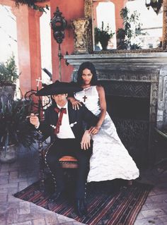 a man and woman sitting on top of a chair in front of a fire place