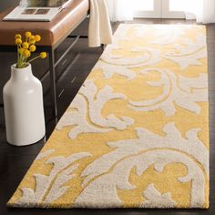 a yellow and white rug in a living room next to a bench with flowers on it