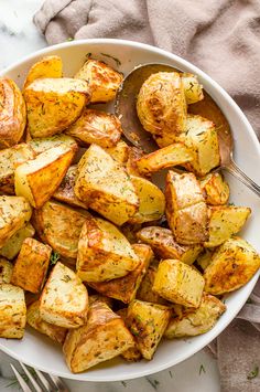 a white bowl filled with cooked potatoes on top of a table next to a fork