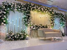 a couch sitting in front of a wall covered with flowers and greenery next to a chair