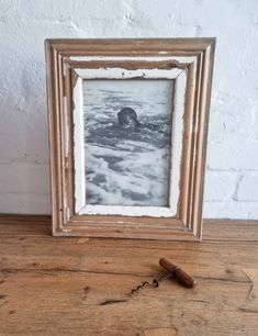 an old photo frame with a corkscrew in front of it on a wooden table