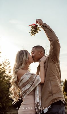 a man and woman kissing each other in front of trees