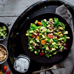 a black plate topped with a salad next to bowls of beans and veggies