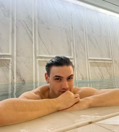 a man laying in a bathtub with his hand on his chin looking at the camera