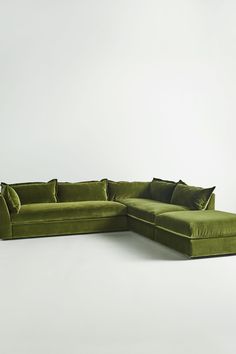 a large green couch with pillows on it's back and side, sitting in front of a white wall