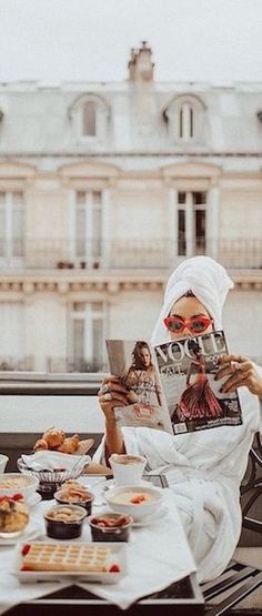 a woman reading a magazine while sitting at a table with pastries and waffles