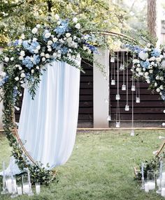 a wedding arch decorated with blue and white flowers, greenery and candles for an outdoor ceremony