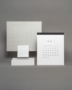 two calendars sitting next to each other on top of a white box with black trim