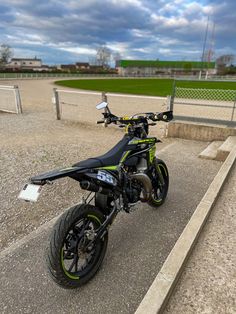 a black and green motorcycle parked on top of a parking lot next to a fence