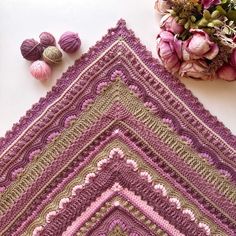 a crocheted afghan next to some flowers and balls of yarn on a table