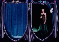 a woman in a black dress standing next to a blue curtain