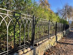 an iron fence with stones on the side and trees in the background