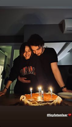 a man and woman standing in front of a cake with lit candles on it that says happy birthday