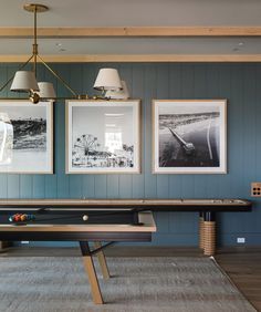 a pool table in a room with two pictures on the wall and a light fixture hanging above it