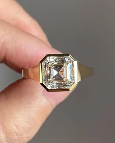 a close up of a person's hand holding a ring with an emerald stone