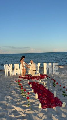 two people are sitting on the beach with flowers and candles in front of them that spell out mam me