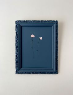 two pink flowers in a blue frame hanging on the wall