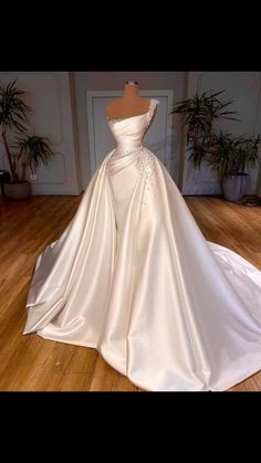 a white wedding dress on display in a room with wooden floors and potted plants