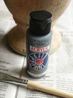 a bottle of acrylic sitting on top of a newspaper next to a brush