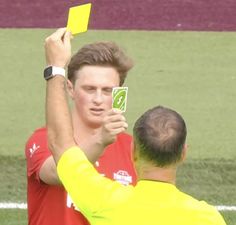 a man holding up a yellow card in front of another man on a soccer field