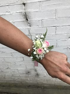 a person's hand holding a bouquet of flowers in front of a brick wall