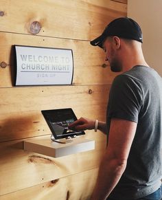 a man standing in front of a wooden wall using a laptop computer