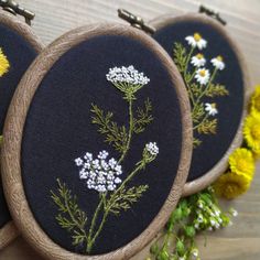 three embroidered hoops with flowers on them sitting next to some yellow and white flowers