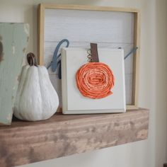 two pumpkins are sitting on top of a shelf next to a frame with an ornament