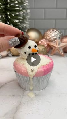 someone is decorating a cupcake with frosting and a snowman on top