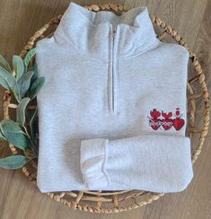 a white sweater with red flowers on it and a plant in the basket next to it