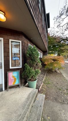 an open sign on the side of a building next to a planter and door