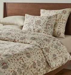 a bed with floral comforter and pillows on top of it in front of a wooden headboard