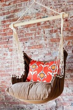 a chair hanging from a brick wall in front of a red and white pillow on a swing