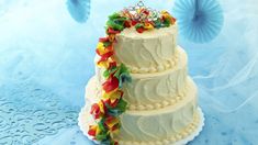 a three tiered wedding cake decorated with colorful ribbons and jewelery on top, sitting on a blue tablecloth