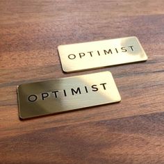 two metal tags that say optimist and optimist on wooden table top