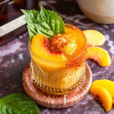 a glass filled with orange juice and garnished with green leaves on the side